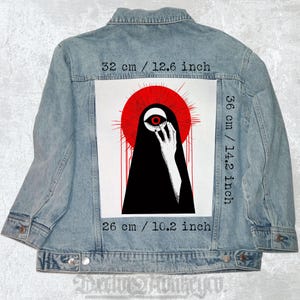 Puede incluir: Una ilustración en blanco y negro de una persona que lleva una prenda negra con capucha, un ojo rojo y un halo rojo. La imagen está impresa sobre un fondo blanco y está rodeada por una chaqueta vaquera. El texto "32 cm / 12.6 inch", "36 cm / 14.2 inch" y "26 cm / 10.2 inch" está impreso en la chaqueta.