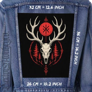 Puede incluir: Una chaqueta vaquera azul con un gran parche rectangular negro en la espalda. El parche muestra un cráneo de ciervo blanco con astas, un sol rojo con una runa negra y pinos rojos. Las dimensiones son de 32 cm por 36 cm.