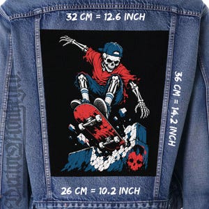 Può includere: Una giacca di jeans blu con una grande toppa rettangolare sulla schiena raffigurante uno scheletro con berretto blu e maglietta rossa, che va sullo skateboard sopra una struttura in pietra. La toppa misura 32 cm per 36 cm.