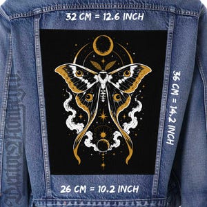 Peut inclure: Une veste en jean bleu avec un grand écusson rectangulaire au dos, présentant un fond noir et une illustration de papillon de nuit dorée et blanche. Le motif inclut des éléments célestes, des étoiles et des nuages. Dimensions : 32 cm par 36 cm par 26 cm.