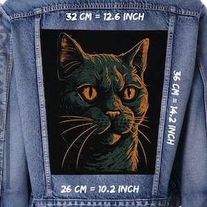 Peut inclure: Veste en jean bleue avec un grand écusson rectangulaire représentant un visage de chat stylisé. Le chat est vert et orange, avec des yeux orange. L'écusson mesure 26 cm de large sur 36 cm de haut.