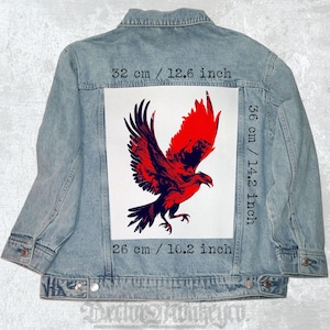 Puede incluir: Chaqueta vaquera azul claro con un gran gráfico de un águila roja y negra en la espalda. El gráfico mide 32 cm de ancho, 36 cm de alto y 26 cm de largo. La chaqueta tiene un diseño clásico con botones.