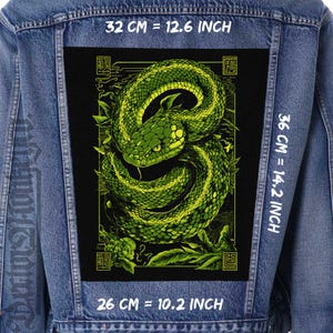 May include: A black and green snake with a Japanese-style design on a denim jacket. The snake is coiled and has a green and yellow pattern. The design is surrounded by a black border and has Japanese characters on the top and bottom. The jacket is blue denim and has white text on the front and back.