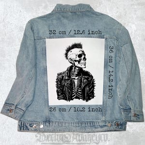 May include: Light blue denim jacket with a large white graphic on the back. The graphic is a black and white illustration of a skull wearing a leather jacket. The graphic measures 12.6 inches wide, 14.2 inches tall, and 10.2 inches long.