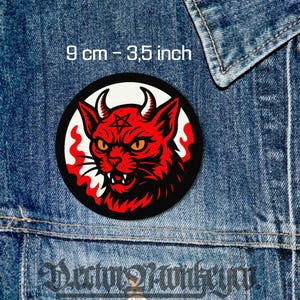 May include: A round patch featuring a red devil cat design with horns, a pentagram, and flames. The patch is 3.5 inches (9 cm) in diameter and is set against a denim background.