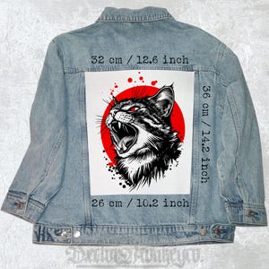 May include: Light blue denim jacket with a large graphic on the back. The graphic features a black and white illustration of a snarling cat with red eyes against a red circle. The graphic measures 12.6 inches wide, 14.2 inches high, and 10.2 inches long.