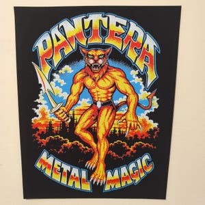 Op de afbeelding: Een zwarte rechthoekige stoffen patch met een centrale gele en oranje antropomorfe panterfiguur die een zilveren zwaard vasthoudt. De tekst PANTERA staat in een boog erboven en METAL MAGIC eronder in gele, oranje en blauwe letters.