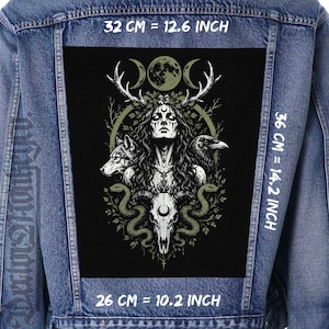 May include: A blue denim jacket featuring a large rectangular black patch on the back. The patch displays a graphic of a figure with antlers, a wolf, a raven, snakes, and a skull with a crescent moon. Text indicates dimensions of 32 cm by 36 cm by 26 cm.
