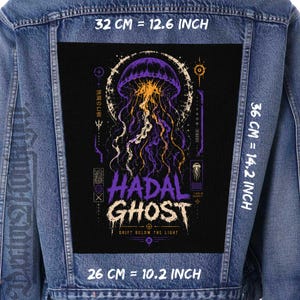 Pode incluir: Um casaco de ganga azul com um grande emblema retangular preto nas costas. O emblema apresenta um gráfico de uma alforreca roxa e laranja com o texto HADAL GHOST e DRIFT BELOW THE LIGHT. As dimensões são 32 cm por 36 cm por 26 cm.