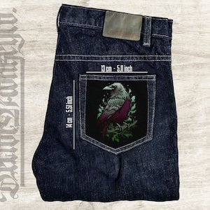 Può includere: Una tasca di jeans blu scuro con una toppa nera che presenta un'illustrazione dettagliata di un corvo bianco con fogliame verde. La toppa misura 13 cm per 14 cm.