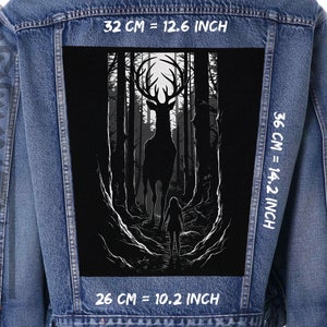 Può includere: Un grafico in bianco e nero di un cervo in piedi in una foresta oscura. Il cervo è in silhouette contro una luna bianca. Il grafico è stampato su una giacca di jeans. La giacca è blu e ha cuciture bianche. Il grafico misura 32 cm per 36 cm, ovvero 12,6 pollici per 14,2 pollici.