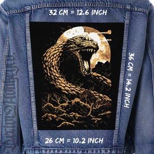 May include: A denim jacket with a large, rectangular patch featuring a detailed illustration of a snake with its mouth open, set against a full moon. The patch measures 12.6 inches by 14.2 inches, and 10.2 inches wide.