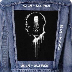 May include: A denim jacket with a large black patch featuring a white illustration of a person's head with a jail cell inside. The patch measures 32 cm wide, 36 cm tall, and 26 cm long.