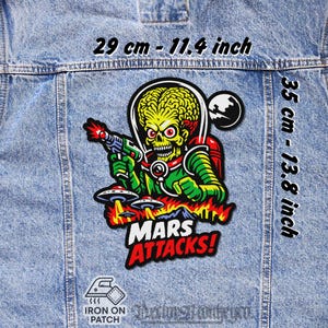 May include: A colorful iron-on patch featuring a green Martian with a ray gun, UFOs, and the text "MARS ATTACKS!". The patch measures 11.4 inches wide and 13.8 inches tall.
