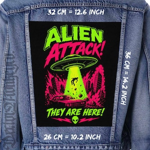 Op de afbeelding: Spijkerjasje met een groot, rechthoekig embleem met een neon groene en roze afbeelding. Het embleem luidt "ALIEN ATTACK! THEY ARE HERE!" en toont een UFO, een persoon die wordt opgetild en een auto. Het embleem meet 32 cm bij 36 cm.