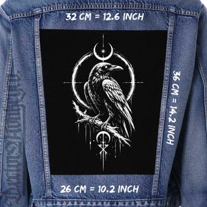 May include: A denim jacket with a large black patch featuring a detailed white illustration of a raven perched on a branch, surrounded by a circular design. The patch measures 32 cm by 36 cm and 26 cm. The jacket has a classic design.