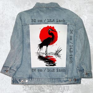 Könnte beinhalten: Eine Schwarzweißillustration eines Reihers, der in einem Teich steht, mit einer roten Sonne dahinter. Die Illustration ist auf weißem Hintergrund und von einer blauen Jeansjacke umgeben. Die Maße der Illustration betragen 32 cm x 36 cm.