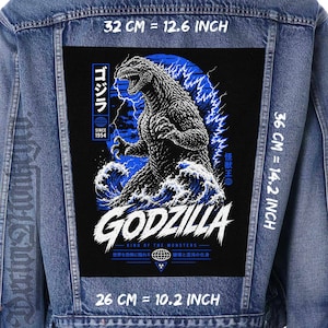 Op de afbeelding: Spijkerjasje met een grote zwarte patch met Godzilla, een monster, in een blauw-witte afbeelding. De patch is 32 cm breed en 36 cm hoog. Tekst bevat "GODZILLA" en "KING OF THE MONSTERS".