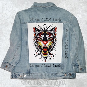 Puede incluir: Chaqueta vaquera azul claro con un llamativo gráfico de cara de tigre en la espalda. El gráfico, de 32 cm de ancho, 36 cm de alto y 26 cm de largo, es una ilustración detallada en rojo, negro y amarillo. La chaqueta tiene un diseño clásico.