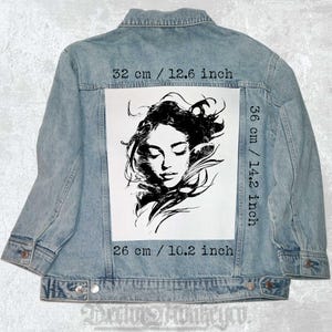 May include: Light blue denim jacket with a black and white graphic of a woman's face on the back. The graphic measures 12.6 inches wide by 14.2 inches high. The jacket's graphic is 10.2 inches in height.