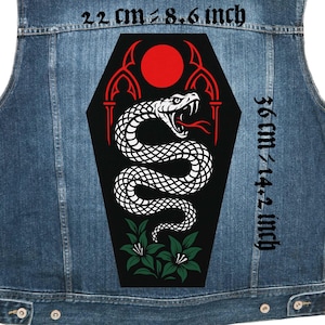 Könnte beinhalten: Eine Jeansweste mit einem großen, schwarzen Aufnäher mit einem weißen Schlangendesign. Der Aufnäher enthält eine rote Sonne, gotische Bögen und grüne florale Akzente. Der Aufnäher misst 22 cm x 36 cm.