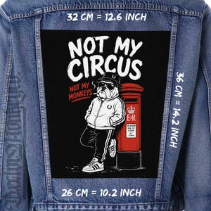 May include: A blue denim jacket featuring a large rectangular back patch with a graphic of a bulldog wearing a bucket hat, sunglasses, and a tracksuit, leaning against a red British post box. The text reads NOT MY CIRCUS NOT MY MONKEYS.