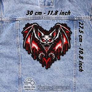 May include: A heart-shaped iron-on patch with a red and white bat-like creature design, measuring 30 cm by 27.5 cm. The creature has glowing eyes and dripping blood details. The text "Iron on Patch" is visible.