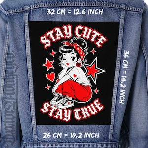 Può includere: Giacca di jeans con una grande toppa nera con una donna dei cartoni animati con pantaloni rossi e una camicia bianca. La toppa recita "STAY CUTE STAY TRUE" con stelle e cuori rossi. La toppa misura 32 cm per 36 cm.