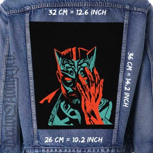 Pode incluir: Casaco de ganga com um grande patch retangular com uma ilustração estilizada de uma pessoa com um design turquesa e laranja. O patch mede 32 cm por 36 cm. O texto no patch diz "Dextors".