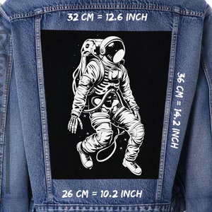 May include: A black and white illustration of an astronaut floating in space. The illustration is printed on a black fabric patch with white text that reads "32 CM = 12.6 INCH", "36 CM = 14.2 INCH", and "26 CM = 10.2 INCH".