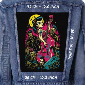 May include: A blue denim jacket featuring a large rectangular back patch with a graphic illustration of a woman playing a pink upright bass surrounded by zombies, a coffin, and a yellow moon. The patch measures 32 cm by 36 cm or 12.6 by 14.2 inches.