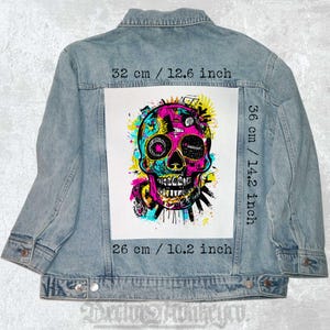 Puede incluir: Un parche gráfico de calavera colorido con un esquema de color rosa, azul, amarillo y verde. El parche mide 26 cm de ancho y 36 cm de alto. Se muestra en una chaqueta vaquera.