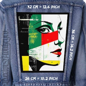 May include: A denim jacket with a colourful abstract portrait patch on the back. The patch features a woman's face with green, red, yellow, and white colours. The text on the jacket reads "32 CM = 12.6 INCH", "36 CM = 14.2 INCH", and "26 CM = 10.2 INCH".