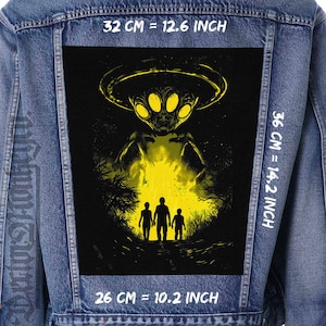 May include: A black and yellow graphic patch of an alien spaceship hovering over three figures in a forest. The patch is sewn onto a blue denim jacket. The text "32 CM = 12.6 INCH", "36 CM = 14.2 INCH", and "26 CM = 10.2 INCH" is printed on the jacket.