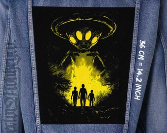 Op de afbeelding: Een zwart en gele grafische patch van een buitenaards ruimteschip dat boven drie figuren in een bos zweeft. De patch is genaaid op een blauw denim jack. De tekst "32 CM = 12.6 INCH", "36 CM = 14.2 INCH" en "26 CM = 10.2 INCH" is op het jack gedrukt.