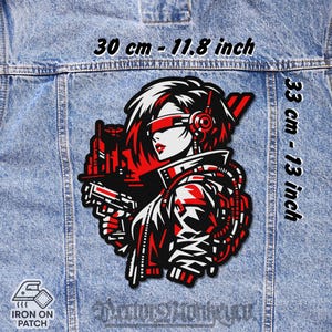 May include: An iron-on patch with a futuristic female figure holding a gun, in black, red, and white. The patch is 30 cm by 33 cm. The text "IRON ON PATCH" is visible.