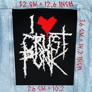 Może przedstawiać: Czarna naszywka z napisem "I Crust Punk" w kolorze białym, z czerwonym sercem. Naszywka ma 32 cm szerokości i 36 cm wysokości, przyszyta do jasnoniebieskiej kurtki dżinsowej.