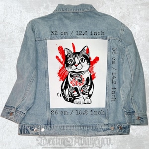 May include: Light blue denim jacket with a large graphic of a black and white cat with red accents. The graphic measures 12.6 inches wide, 14.2 inches tall, and 10.2 inches long. The jacket has a button-down front and two chest pockets.