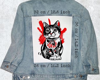Peut inclure: Veste en jean bleu clair ornée d'un motif de chat noir et blanc avec des touches de rouge. Le motif mesure 32 cm de large, 36 cm de haut et 26 cm de long. La veste a une fermeture boutonnée et deux poches poitrine.