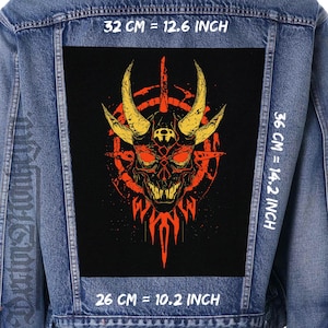 Könnte beinhalten: Jeansjacke mit einem großen, rechteckigen Aufnäher mit einem detaillierten orange-gelben Schädeldesign auf schwarzem Hintergrund. Der Aufnäher ist 32 cm breit, 36 cm hoch und 26 cm lang.