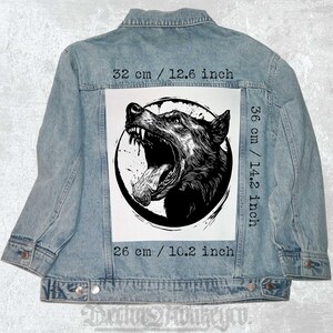 May include: A denim jacket with a black and white graphic of a snarling wolf's head on the back. The graphic is 14.2 inches tall and 10.2 inches wide. The jacket is 12.6 inches wide and 14.2 inches tall.