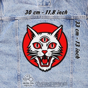 Op de afbeelding: Een opstrijkbare patch met een witte kat met drie rode ogen en een grijnzende mond, tegen een rode cirkel. De patch meet 30 cm bij 33 cm en wordt getoond op een spijkerjasje.