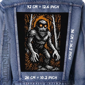 Può includere: Giacca di jeans blu con una grande toppa rettangolare. La toppa raffigura un'illustrazione in bianco e nero di una creatura simile a Bigfoot in un bosco. Misura 32 cm di larghezza, 36 cm di altezza e 26 cm di lunghezza.