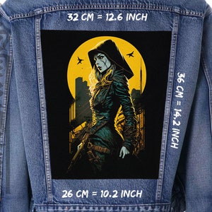 Puede incluir: Un parche gráfico negro y amarillo con una mujer con una capa con capucha de pie en una ciudad con una luna amarilla en el fondo. El parche mide 26 cm de ancho, 36 cm de alto y 32 cm de largo.