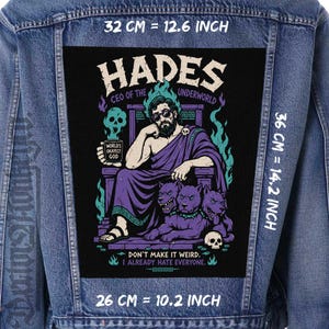 May include: A blue denim jacket featuring a large rectangular back patch with a graphic of Hades sitting on a throne with a three-headed dog. The text reads HADES CEO OF THE UNDERWORLD, WORLD'S OKAYEST GOD, and DON'T MAKE IT WEIRD. I ALREADY HATE EVERYONE. Measures 12.6 by 14.2 inches.