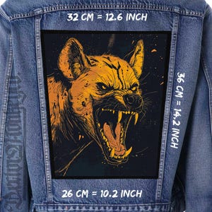 Op de afbeelding: Een zwarte en gele afbeelding van een grommende hyena op een spijkerjack. De afbeelding is 32 cm breed en 36 cm hoog.