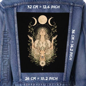 May include: A blue denim jacket featuring a large rectangular patch on the back. The patch displays a black background with a central illustration of a person with arms raised, a deer, and moon phases. Dimensions are 12.6 inches by 14.2 inches by 10.2 inches.