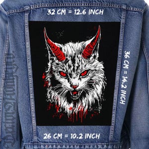 以下が含まれることがあります： 黒い背景に赤い角と目をつけた猫の白黒イラスト。猫は口を開けて牙をむき出しにしてうなり声をあげている。画像は幅32cm、高さ36cm、奥行き26cmです。