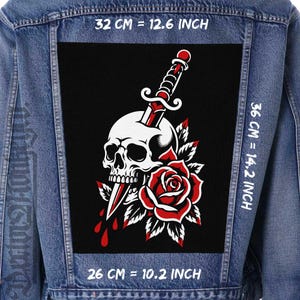 May include: A blue denim jacket featuring a large rectangular back patch with a black background. The patch displays a white skull pierced by a dagger, accompanied by a red rose. Dimensions are 32 cm by 36 cm, or 12.6 inches by 14.2 inches.