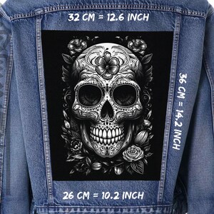 May include: A black and white iron-on patch featuring a detailed sugar skull design with floral accents. The patch measures 12.6 inches wide by 14.2 inches tall.